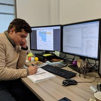 Dr Amir Enshaei writing on a note pad with three computer screens around him
