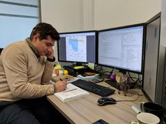 Dr Amir Enshaei writing on a note pad with three computer screens around him