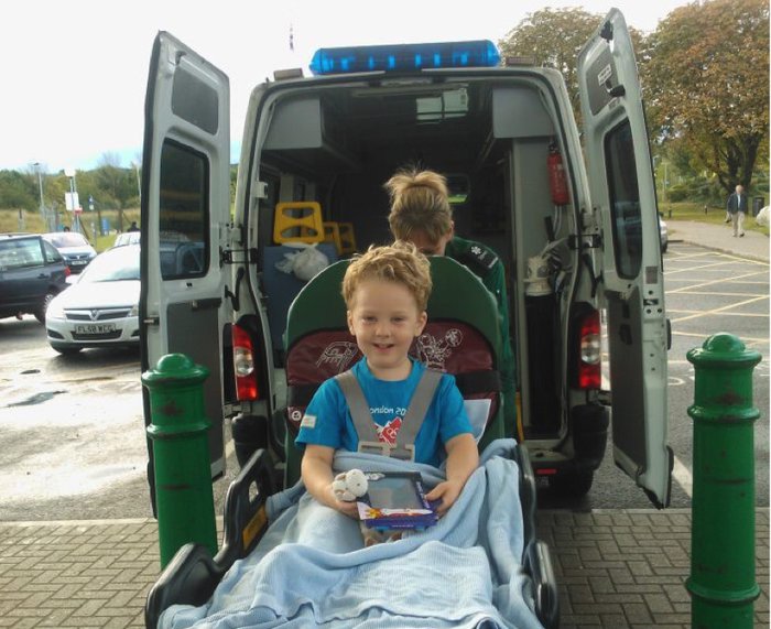 A child sits happy and beaming in a bed as he's loaded into an ambulence.