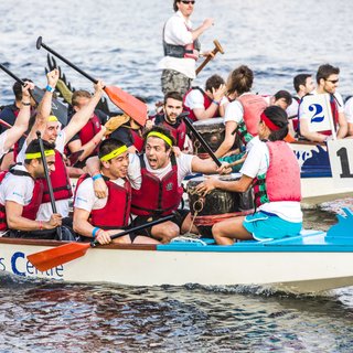 A boat race team, holding paddles as they float on the water, cheering and celebrating after the race.