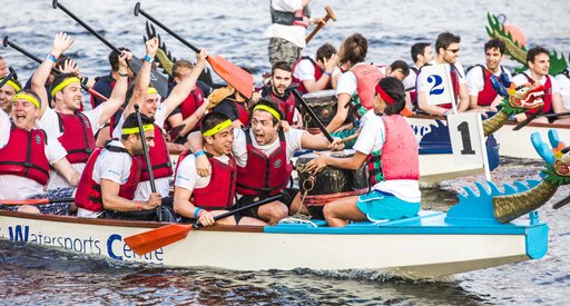 A boat race team, holding paddles as they float on the water, cheering and celebrating after the race.