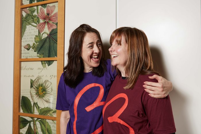 Two women in Blood Cancer UK t-shirts smile together, one has her arm around the other.