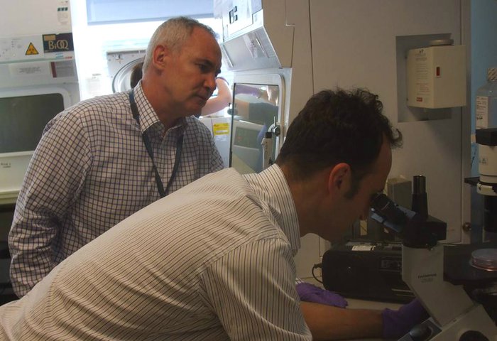 Researcher Brian Huntly observing a colleague looking into a microscope