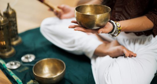 A person sitting cross legged holding a Tibetan bowl and stick.