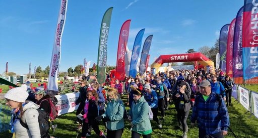 A colourful crowd sets off from the starting line of the Easter 50 ultra challenge. It is a bright spring day and various charity flags are flying in the breeze.