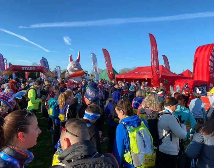 A large crowd of people taking part in the Easter 50 ultra challenge event. It is a sunny spring day and there is an inflatable Easter bunny among the crowd.