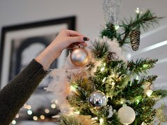 A woman's hand placing a bauble on a Christmas tree.