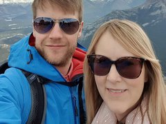 A young couple pose for a phone selfie on holiday, with snow-capped mountains in the background.