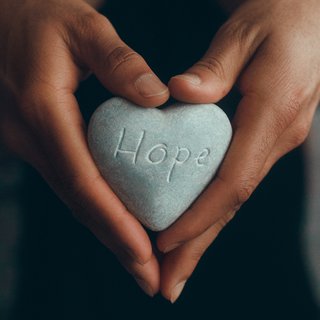Image of hands holding a heart-shaped stone with the word "hope" carved on it.