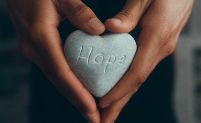 Image of hands holding a heart-shaped stone with the word "hope" carved on it.