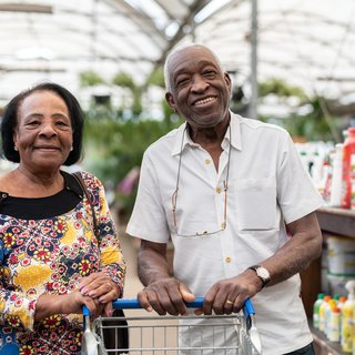 A couple stood with a trolley at a garden centre smiling.