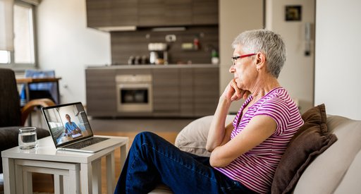 A woman with short grey hair sitting on the sofa in a living room, on a video call with someone on her laptop.