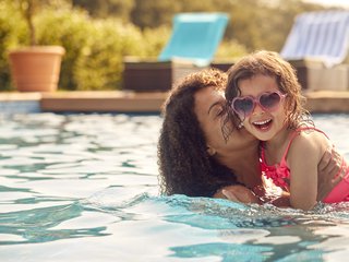 A mother and young daughter smile in a pool on a summer holiday