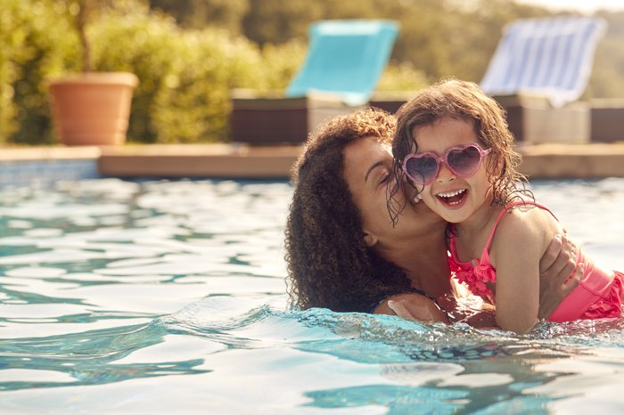 A mother and young daughter smile in a pool on a summer holiday