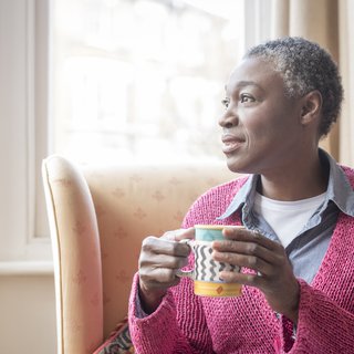 Older Black woman holding mug and looking into the distance