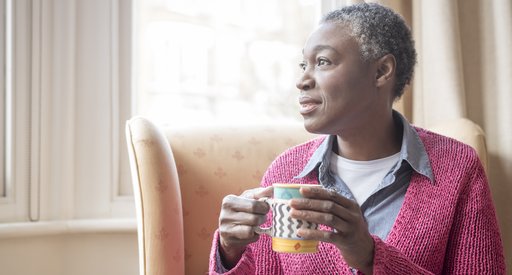 Older Black woman holding mug and looking into the distance