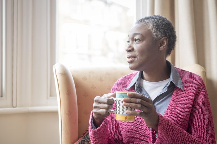 Older Black woman holding mug and looking into the distance