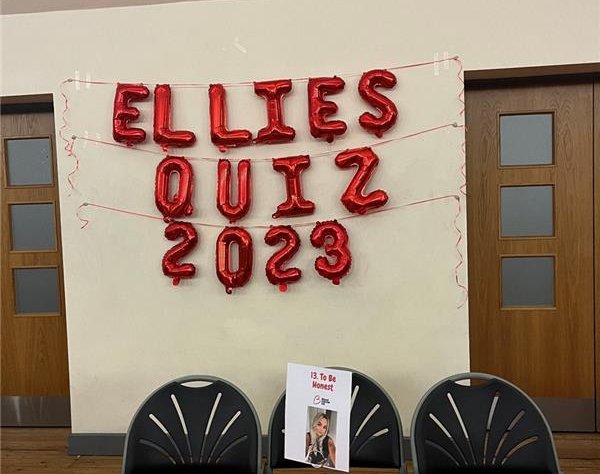 A banner that says 'Ellie's Quiz 2023' in red balloons with a red tablecloth.