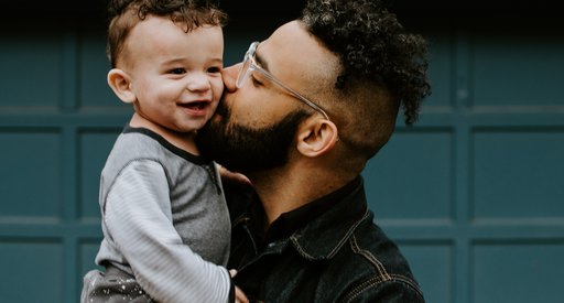 A stock image of a father holding his smiling child up in the air and kissing his cheek.