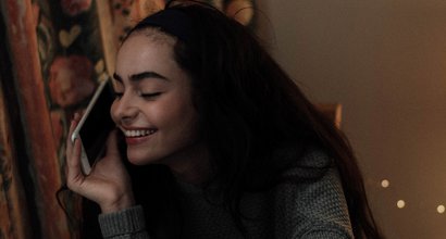 A stock image of a woman smiling while on the phone in a dimly lit room.