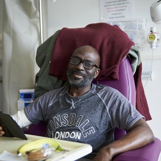 A man sitting in a chair in hospital, with medical equipment around him.