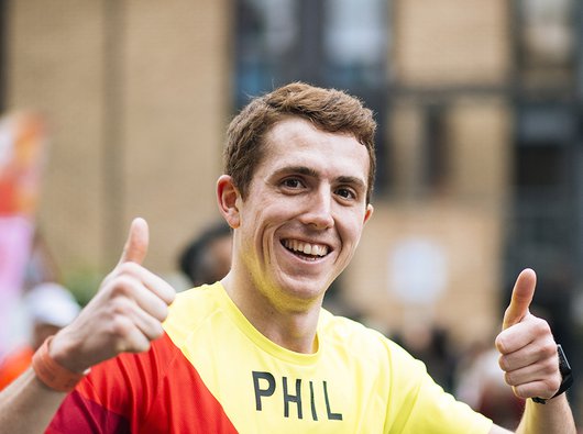 A close up image of a marathon runner holding both thumbs up, grinning at the camera.