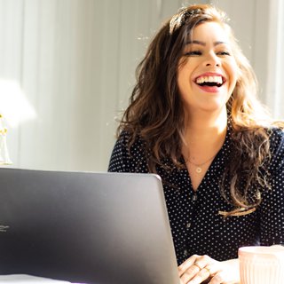 A stock image of a woman laughing as she looks up from her laptop.