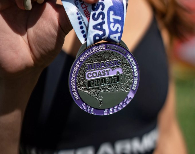 A close up of a medal from the Jurassic Coast Challenge. The medal is blue and silver and has 'Jurassic Coast Challenge Finisher' written on it.