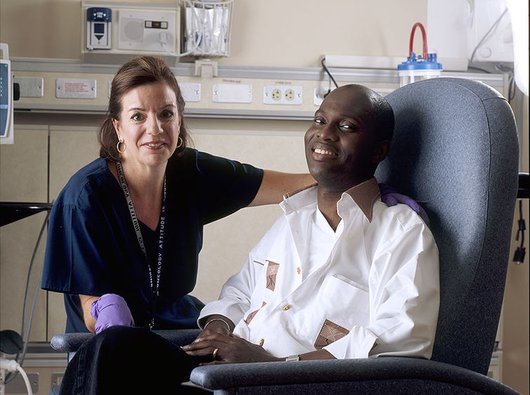 A nurse and a blood cancer patient sit together in a treatment room in a hospital.