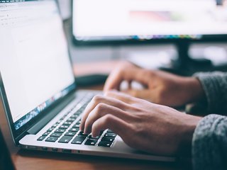 A close up of a person sat at a desk typing on a computer