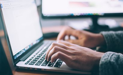 A close up of a person sat at a desk typing on a computer