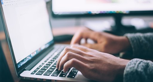 A close up of a person sat at a desk typing on a computer