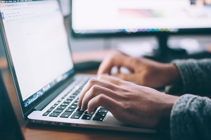 A close up of a person sat at a desk typing on a computer
