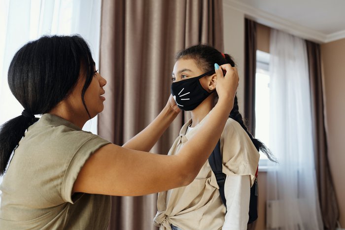 A woman puts a face mask on a child in a house