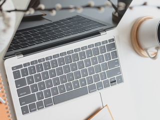 A close up of a laptop with a paper notepad on the keyboard and a person holding a pencil about to write.