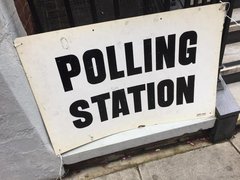 A close up of a sign saying polling station attached to railings on a street