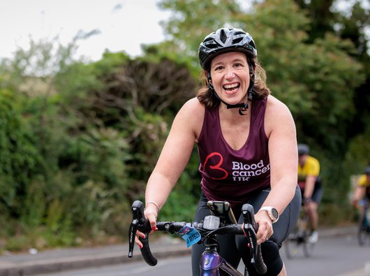 A woman smiles at the camera as she cycles through the countryside