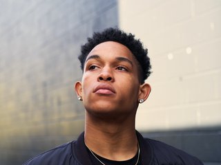 Young person looking upwards with a thoughtful expression in front of a brick wall.