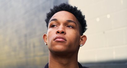 Young person looking upwards with a thoughtful expression in front of a brick wall.