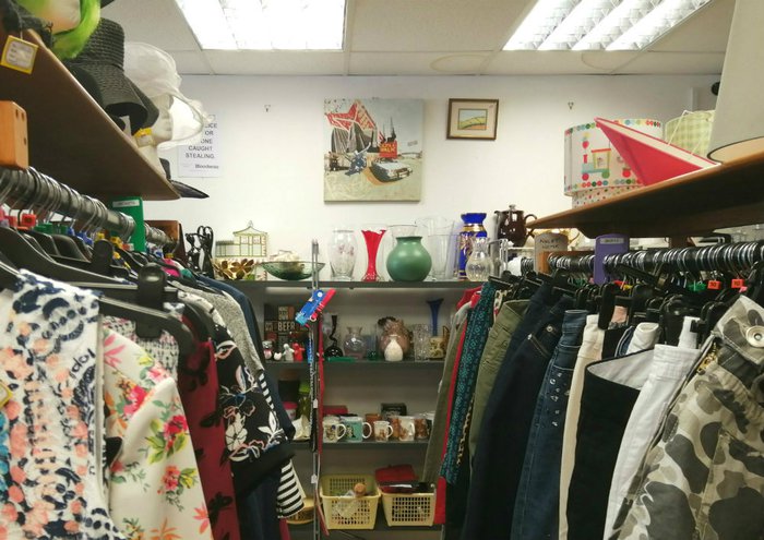 Clothes rails in a charity shop and shelves holding vases and other nik-naks.