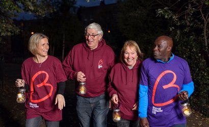 A group of supporters take part in Walk of Light, a night time walk, wearing Blood Cancer UK T-shirts in burgundy and purple. They smile and laugh with each other, enjoying the event.