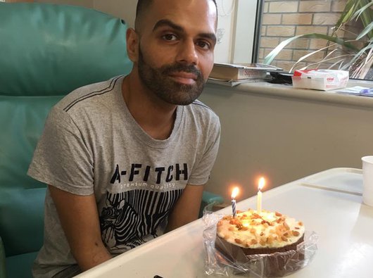 A man named Sunny celebrates his birthday with a cake holding two lit candles.