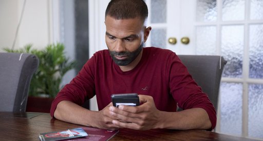 A man sitting at a table, with Blood Cancer UK booklets in front of him. He's holding his phone, as if about to search for something or dial a number.