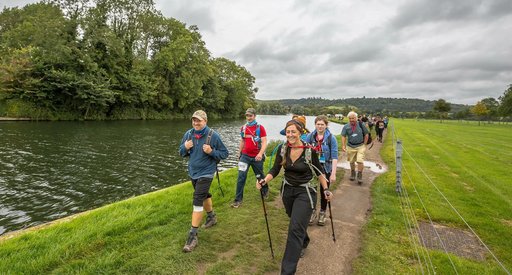 A group of walkers walk the Thames path. They have hiking gear and are walking along the banks of the Thames in the countryside.