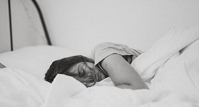 Young adult sleeping under duvet in bed with long hair over face.